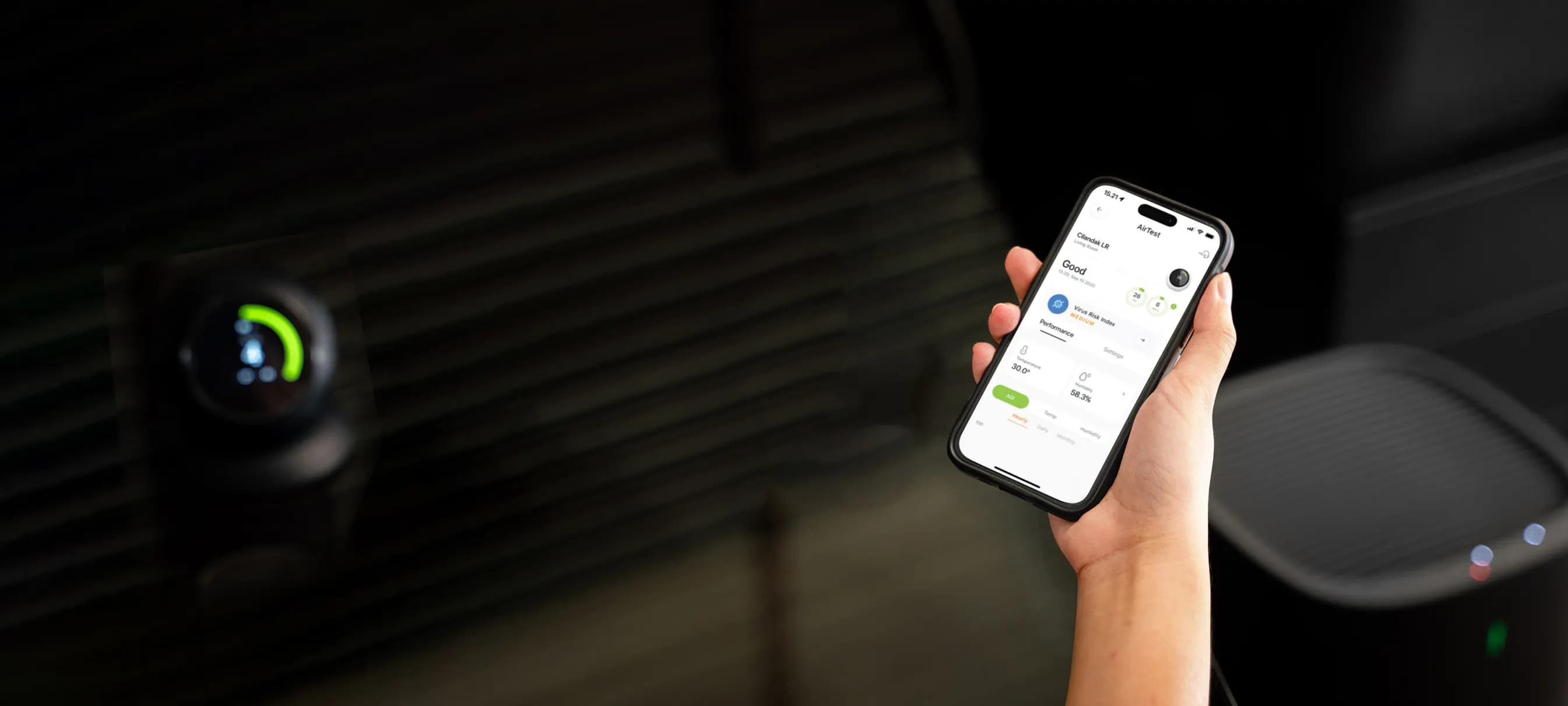 Tangan memegang smartphone yang menampilkan aplikasi ecoCare Pure Air di samping sensor dan purifier